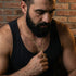 Bearded man in a singlet looking down wearing barbed cross gold steel necklace.