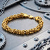 Byzantine chain men's gold steel bracelet on metal bench.