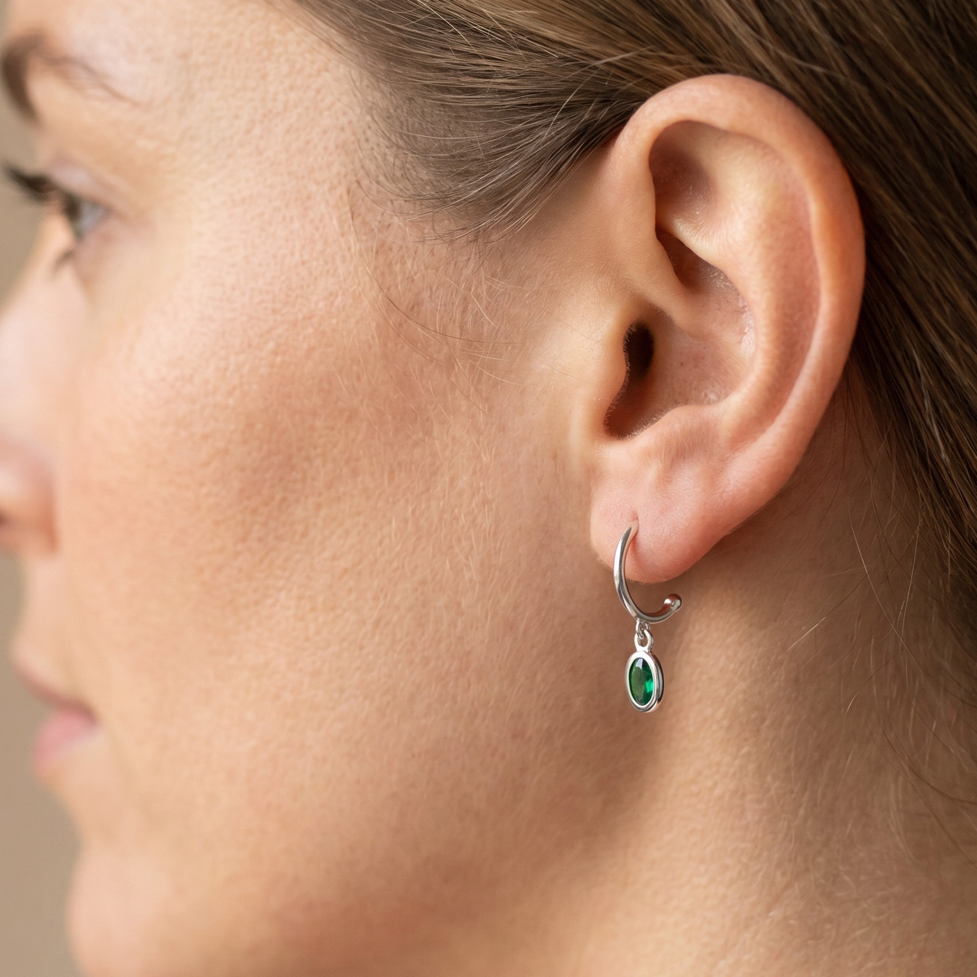 Close-up of woman wearing Engelsrufer green CZ hoop dangle earrings.