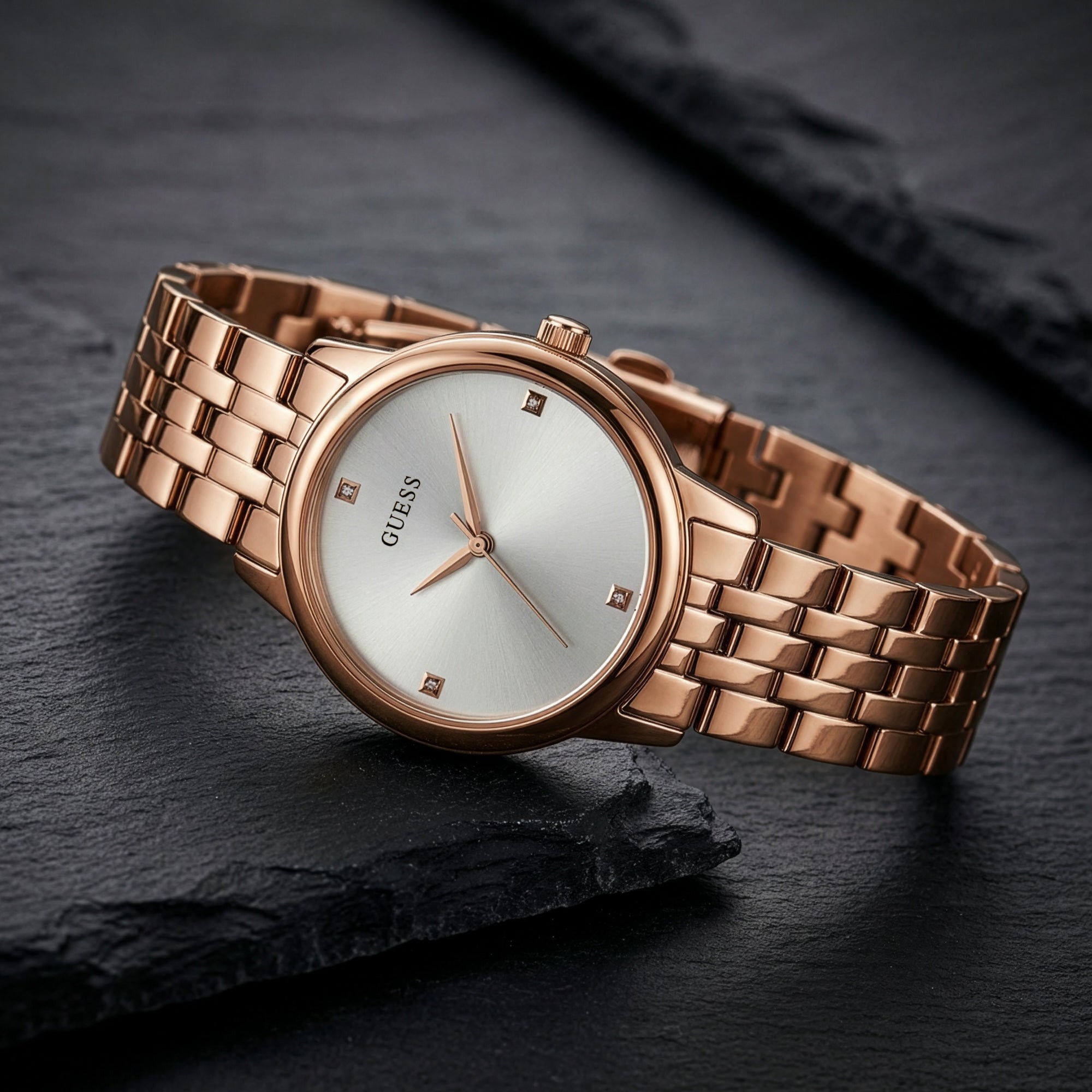 Guess Lady Wafer rose gold dress watch on black rock background.
