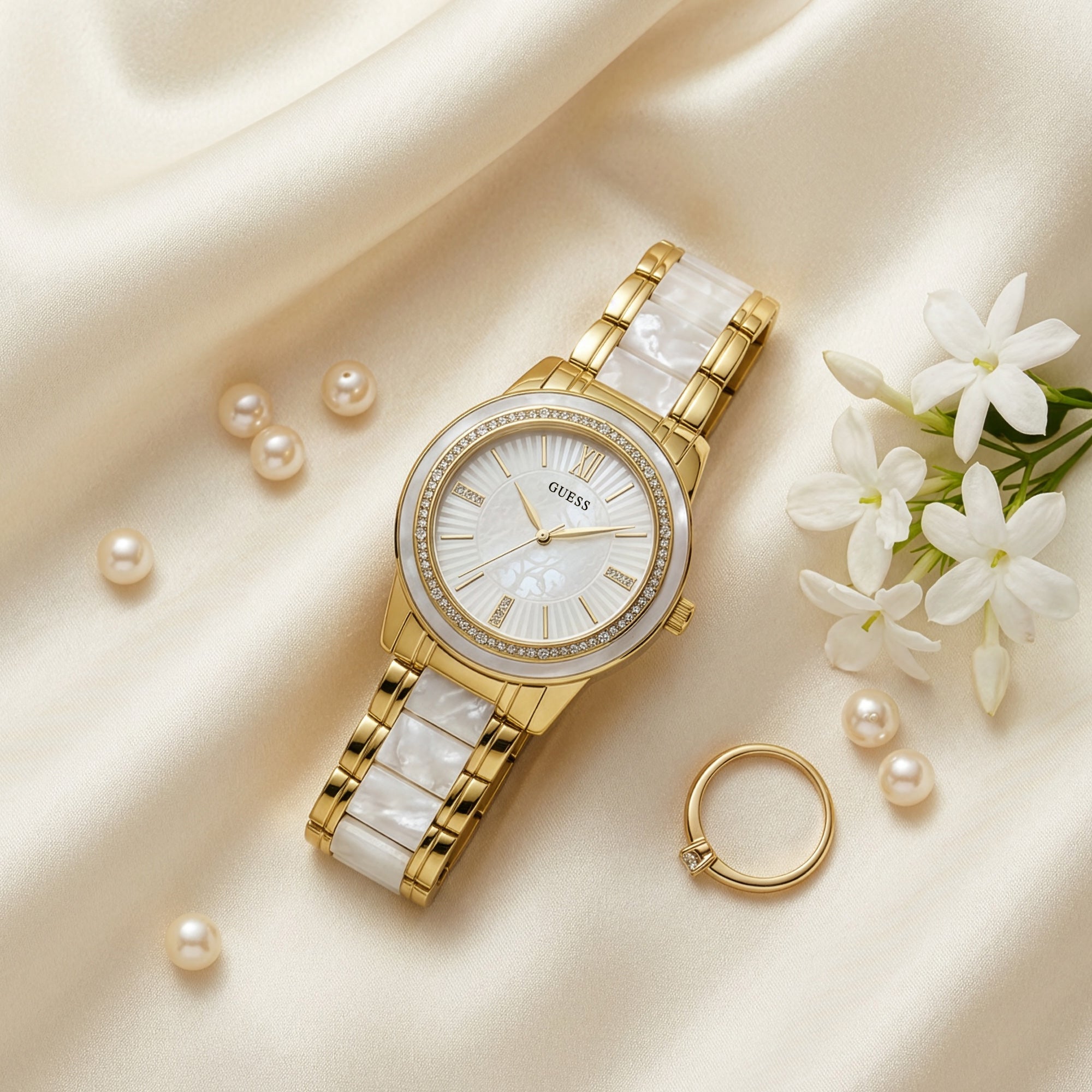 Guess Trinity gold dress sport watch on white fabric with jewellery and flowers.