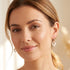 Woman wearing a pair of sterling silver rose gold white ceramic heart earrings.