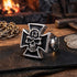 An Iron Cross skull lucky 13 stainless steel men's ring sitting on a strip of leather on a wooden table with an old stone cabin fireplace in the background.