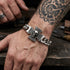 Man with a tattooed arm wearing an Iron Cross skull Cuban link stainless steel bracelet.