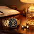 JAG Acton men's black dial gold watch on a wooden desk with a journal, cufflinks and a whisky glass.
