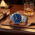 JAG Albany men's blue dial silver watch on a wooden desktop in a man's study.