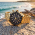 JAG Boss black dial gold men's chronograph watch on a foreshore rock at the beach with the ocean in the background.