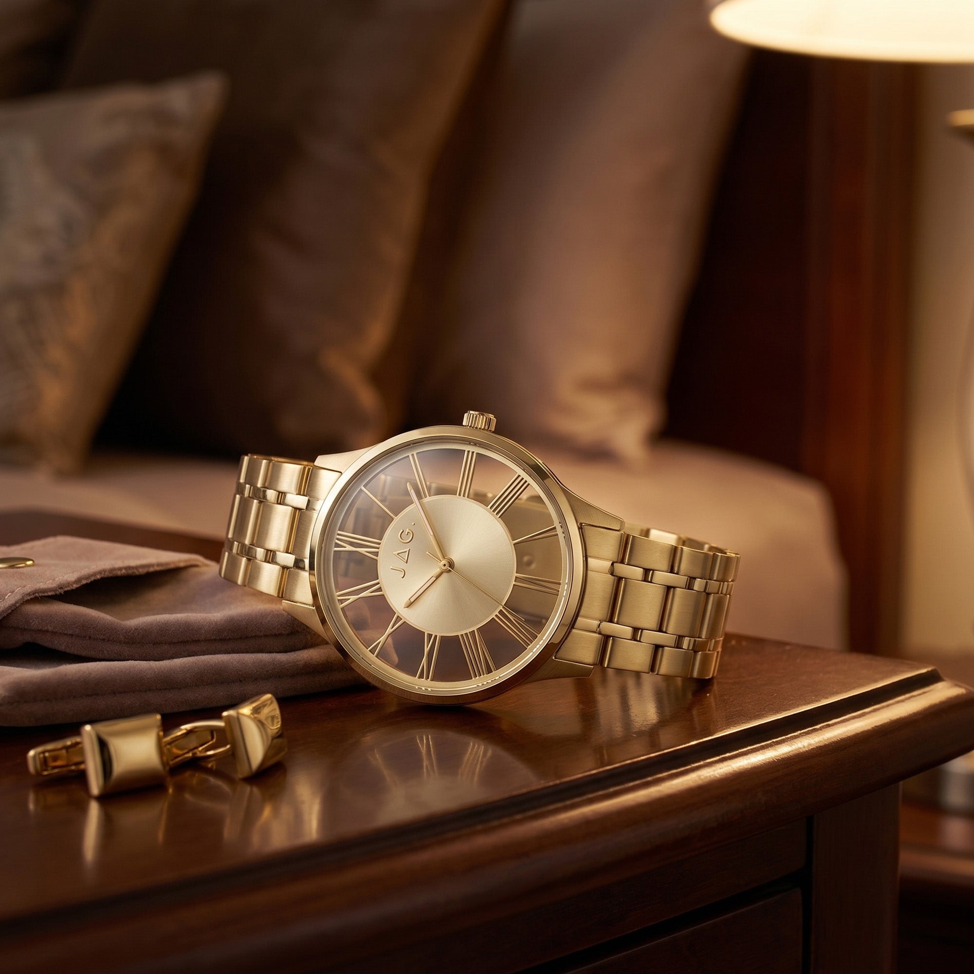 JAG Gerroa gold transparent men's watch laying on a wooden side table with gold cufflinks.