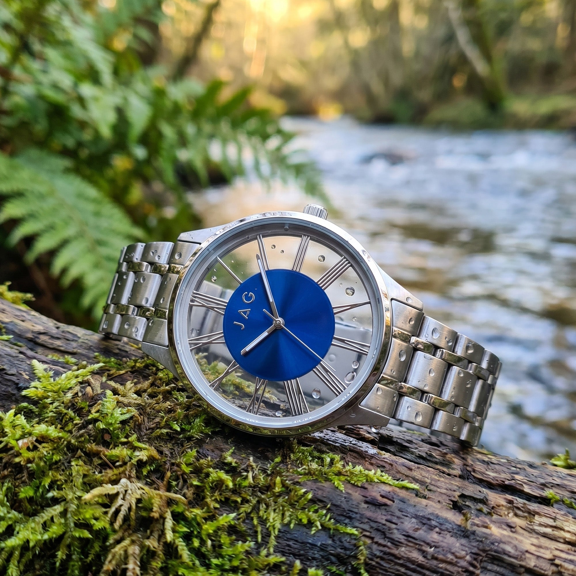 JAG Gerroa silver blue dial transparent watch laying on a moss-covered log near a river.