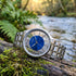 JAG Gerroa silver blue dial transparent watch laying on a moss-covered log near a river.