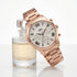 JAG ladies Estelle rose gold watch resting against a perfume bottle.