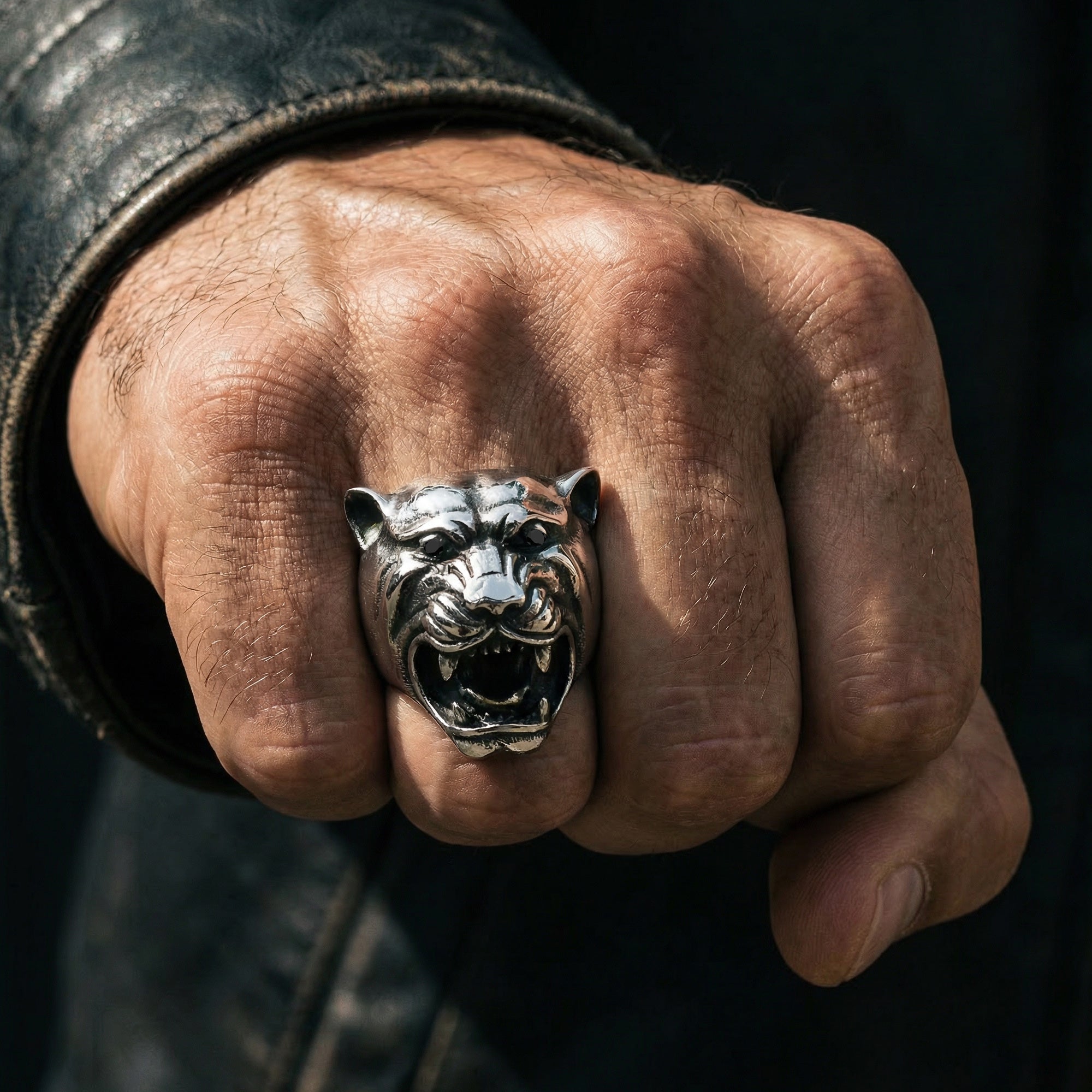 Man's hand making a fist wearing a snarling jaguar head stainless steel ring.