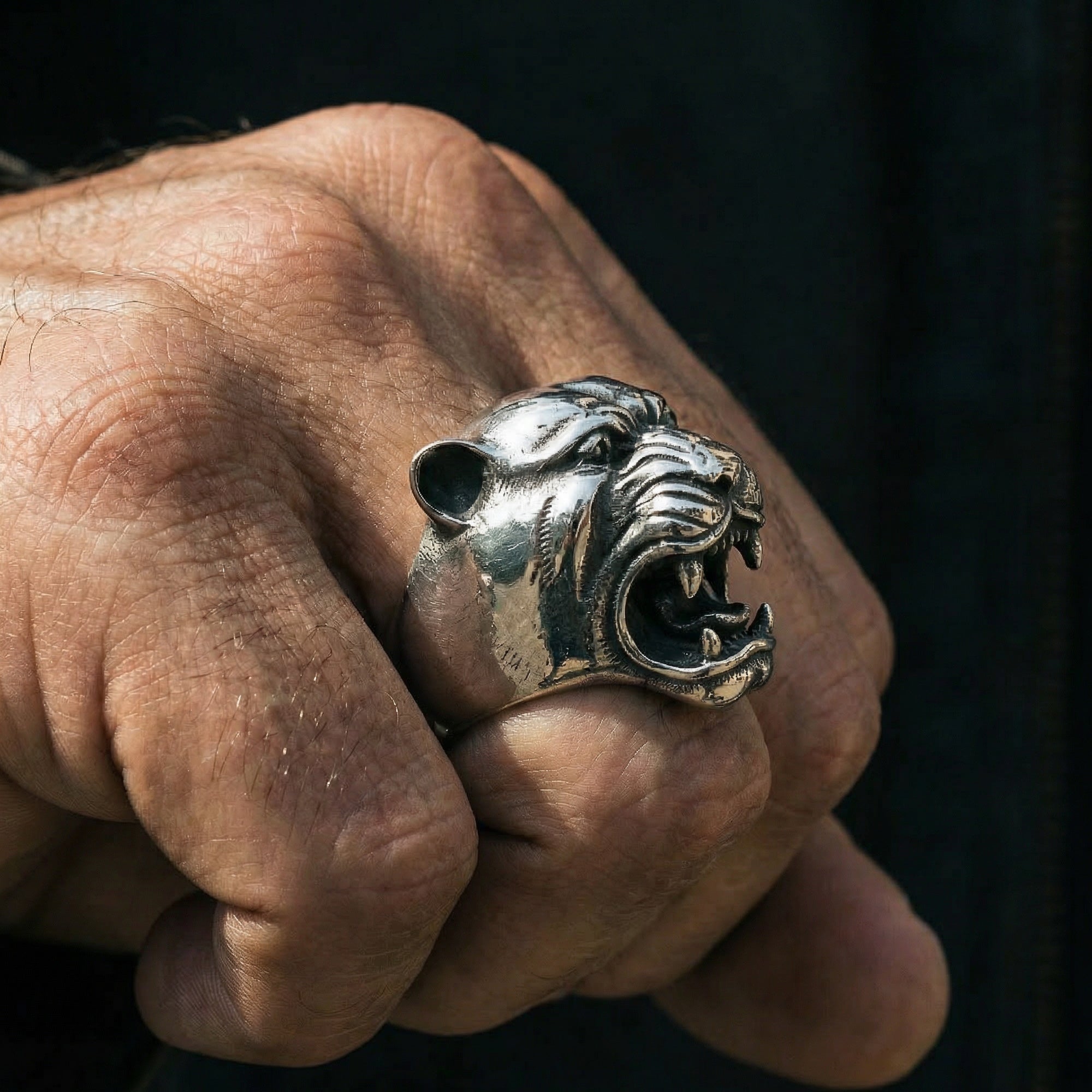 Side view of man's hand making a fist wearing a snarling jaguar head stainless steel ring.