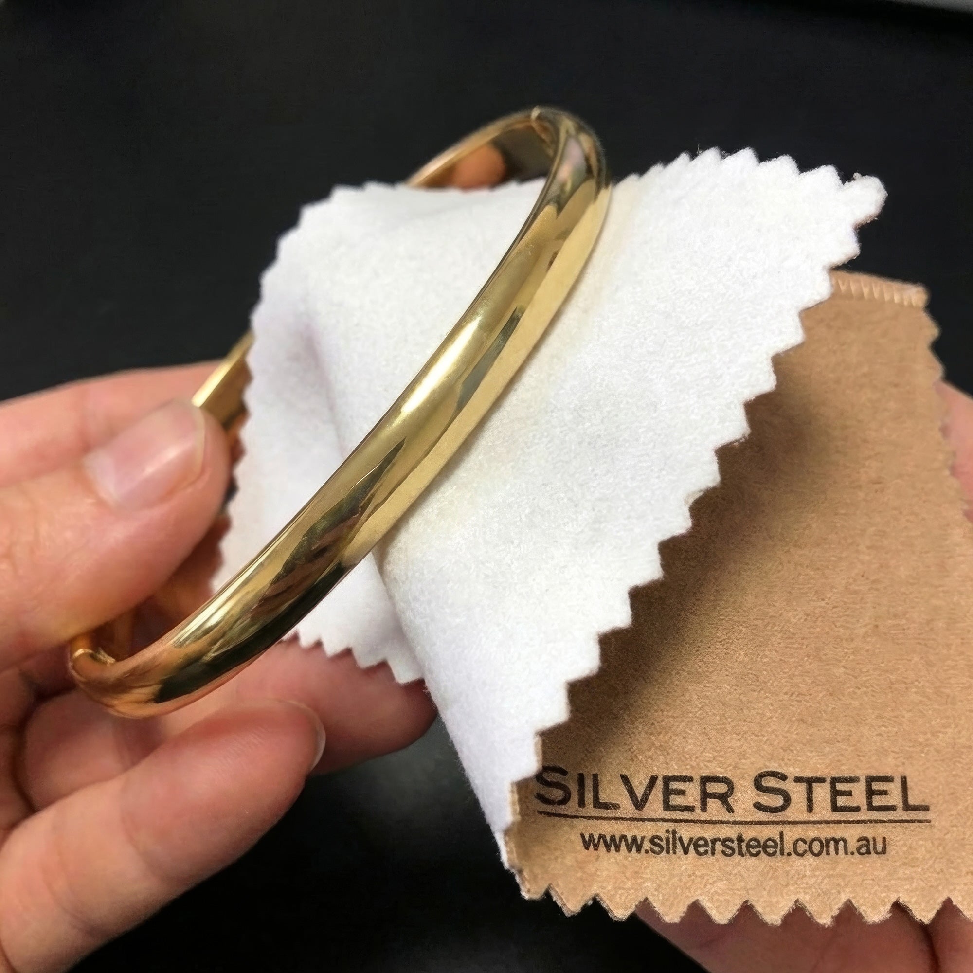 Gold bangle being polished with a jewellery cleaning and polishing cloth.