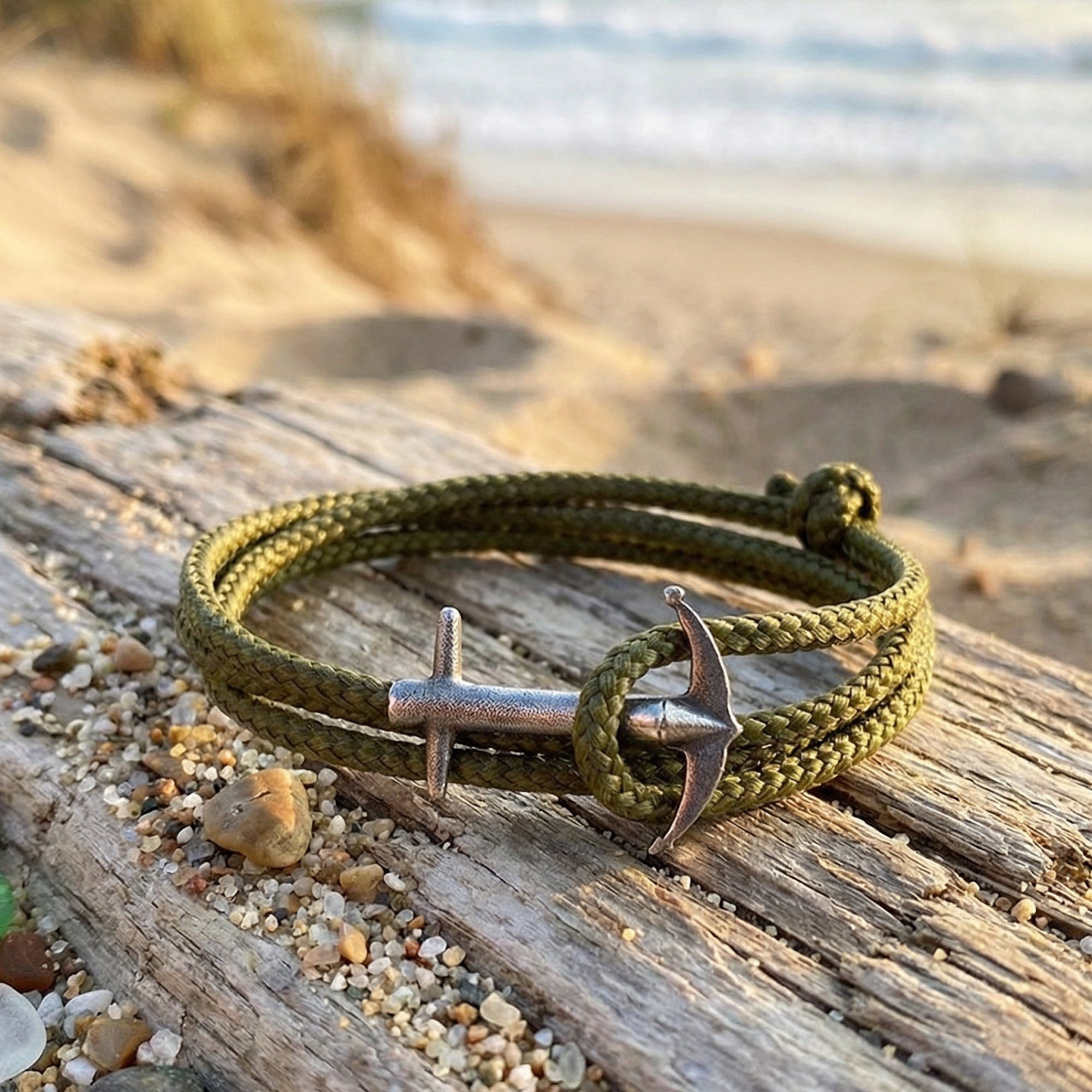 Anchor & Crew Admiral silver khaki green rope bracelet on a wooden step near the beach.