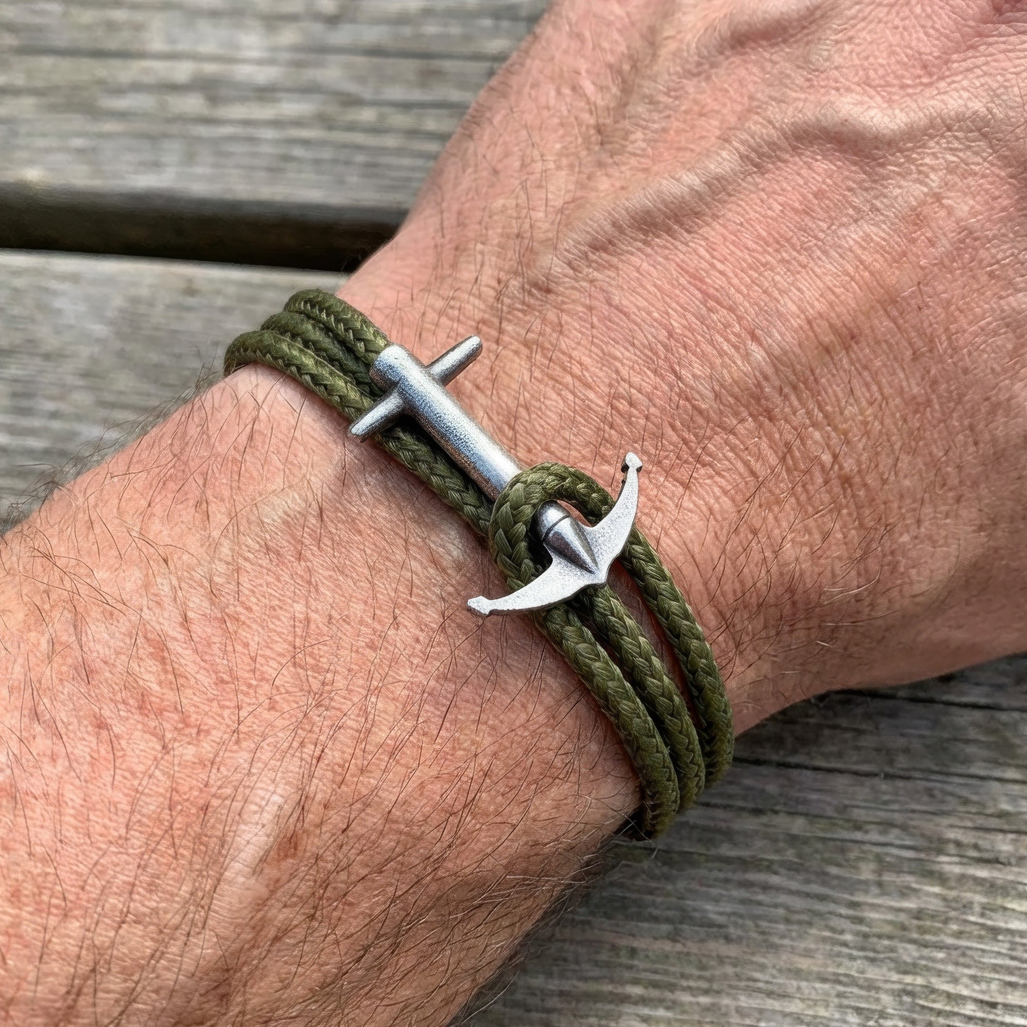 Close-up of man wearing Anchor & Crew Admiral silver khaki green rope bracelet on wrist.