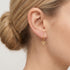 Close-up of woman wearing Engelsrufer little angel gold hoop earrings.
