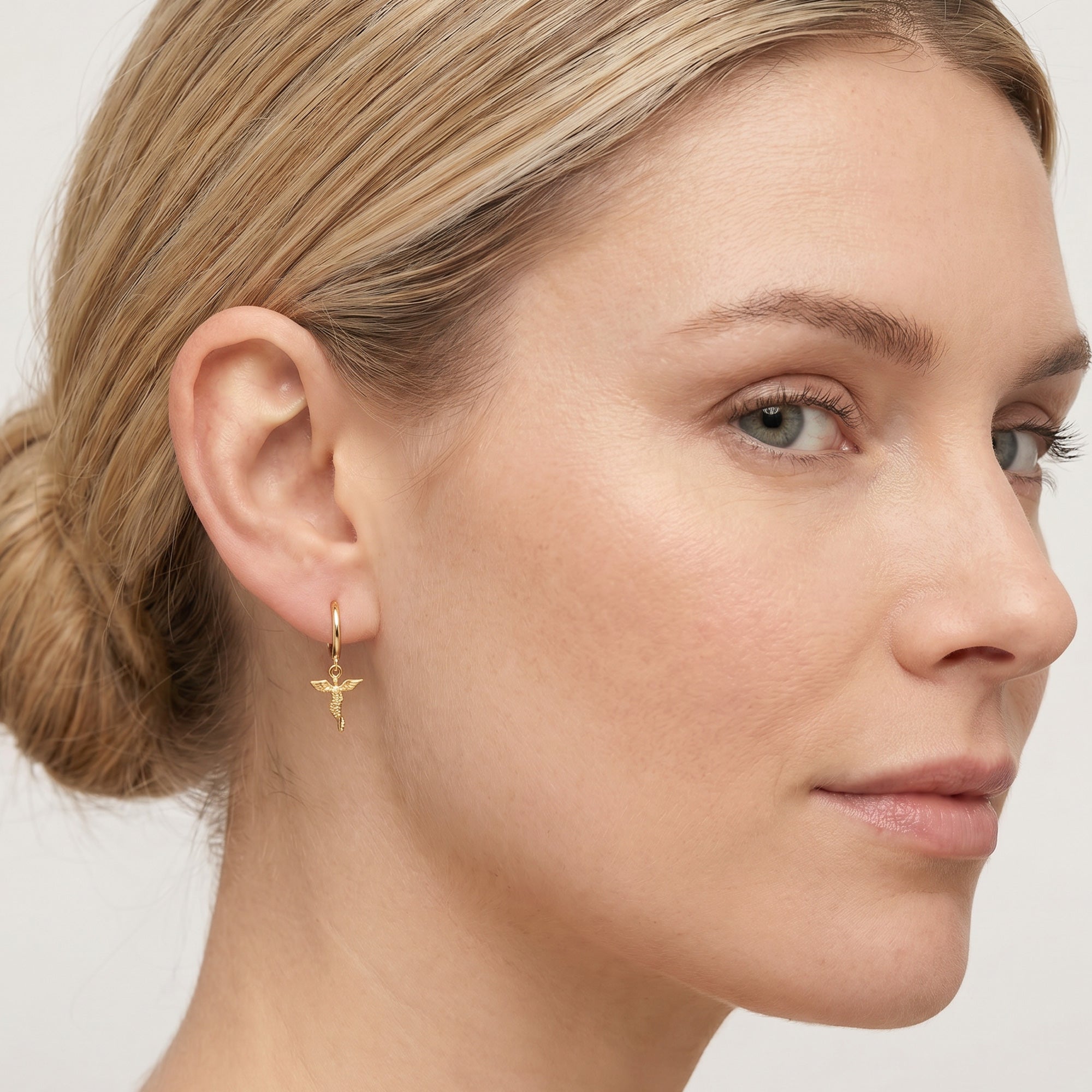 Woman wearing Engelsrufer little angel gold hoop earrings.