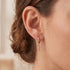 Close-up of woman wearing Engelsrufer little angel rose gold hoop earrings.
