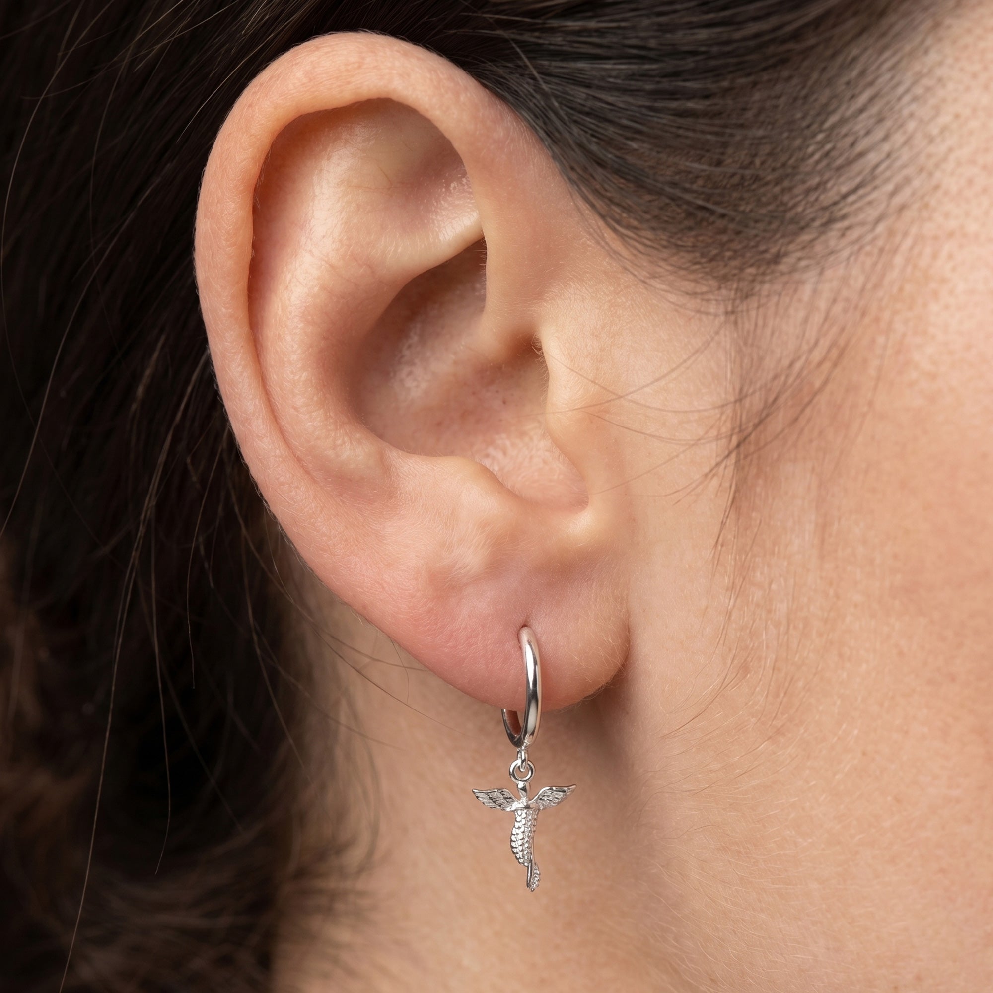 Woman wearing Engelsrufer little angel silver hoop earrings.