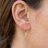 Close-up of woman wearing Engelsrufer little feather gold hoop earrings.