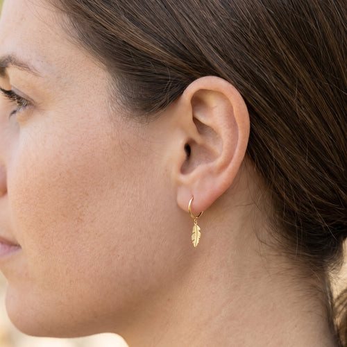 Woman wearing Engelsrufer little feather gold hoop earrings.