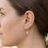 Woman wearing Engelsrufer little feather gold hoop earrings.