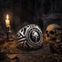 A memento mori skull stainless steel signet ring sitting on a decrepit wooden table next to a skull and burning candle in a crypt.