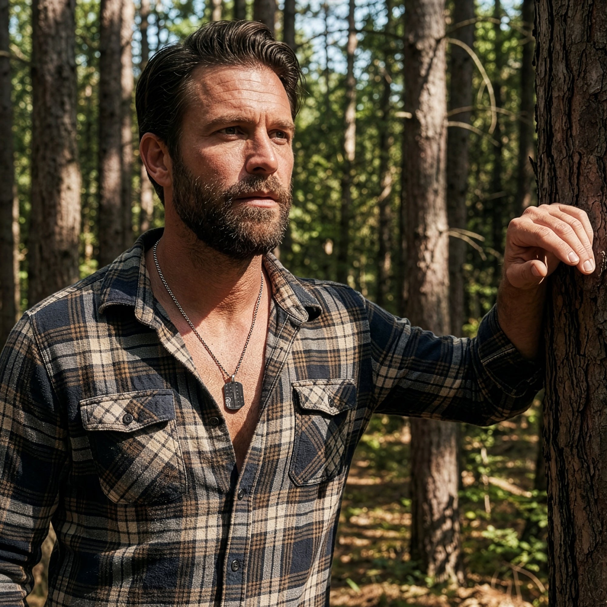 Man in an open-neck shirt leaning against a tree in the forest wearing military star dog tag necklace.