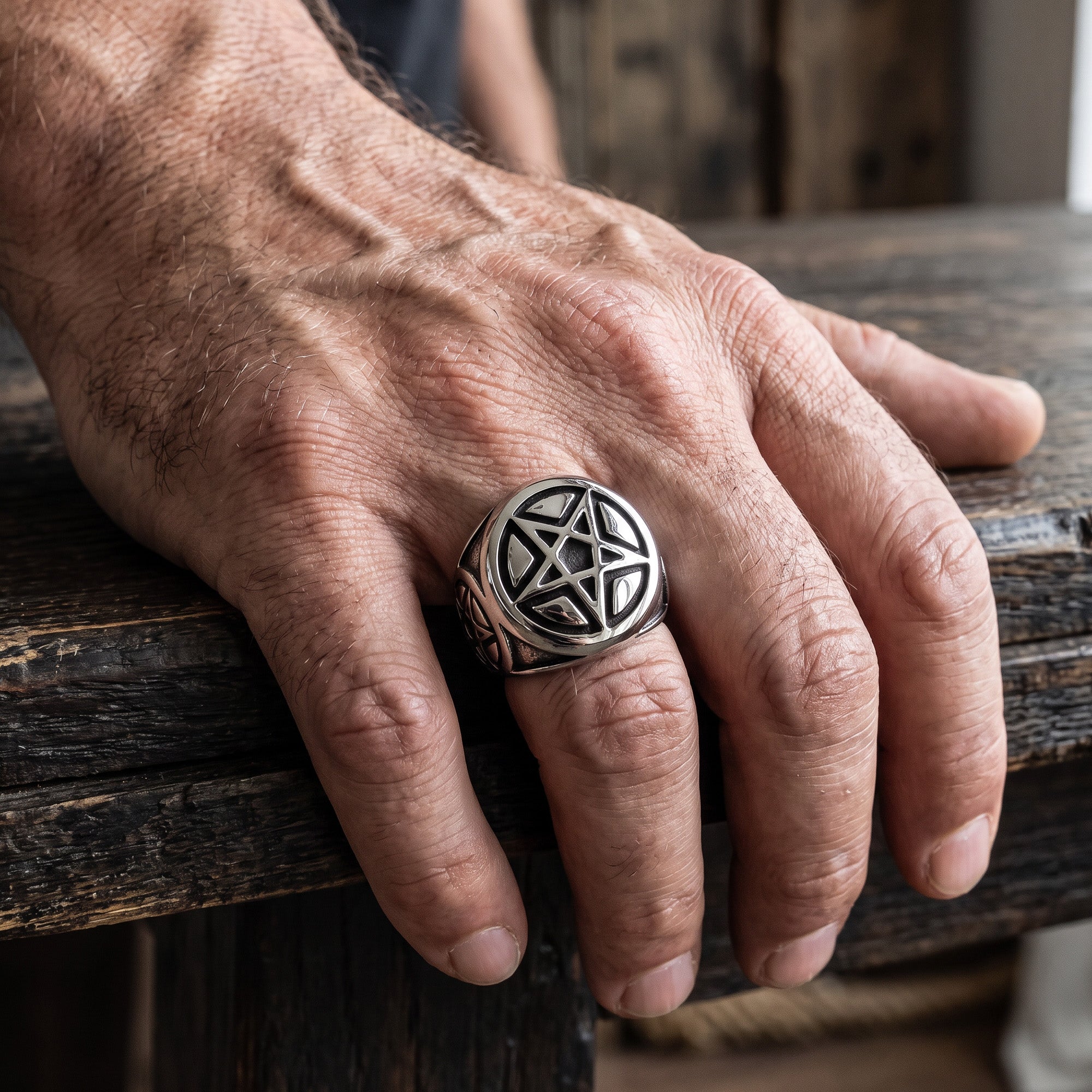 Man wearing a pentagram stainless steel signet ring while resting his hand on a wooden table.