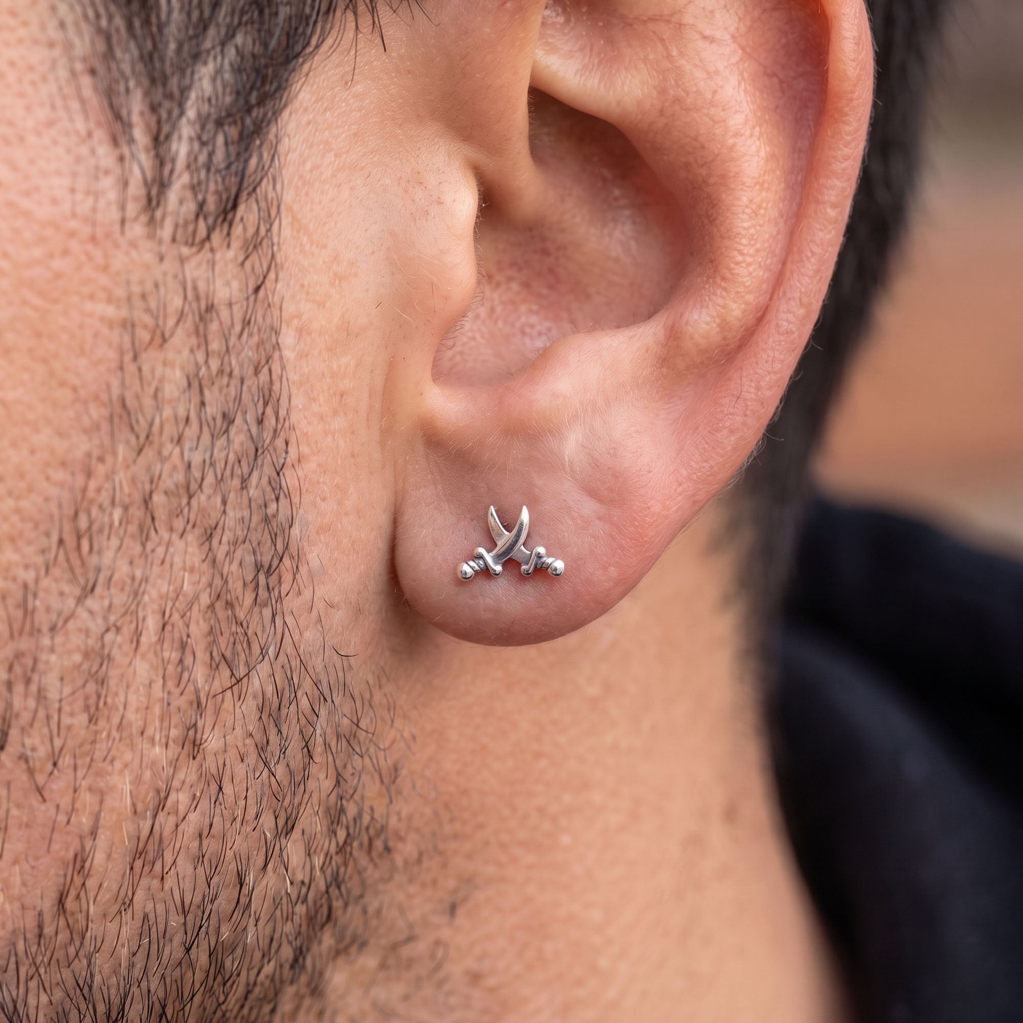 Close-up of man wearing pirate swords stainless steel stud earring.