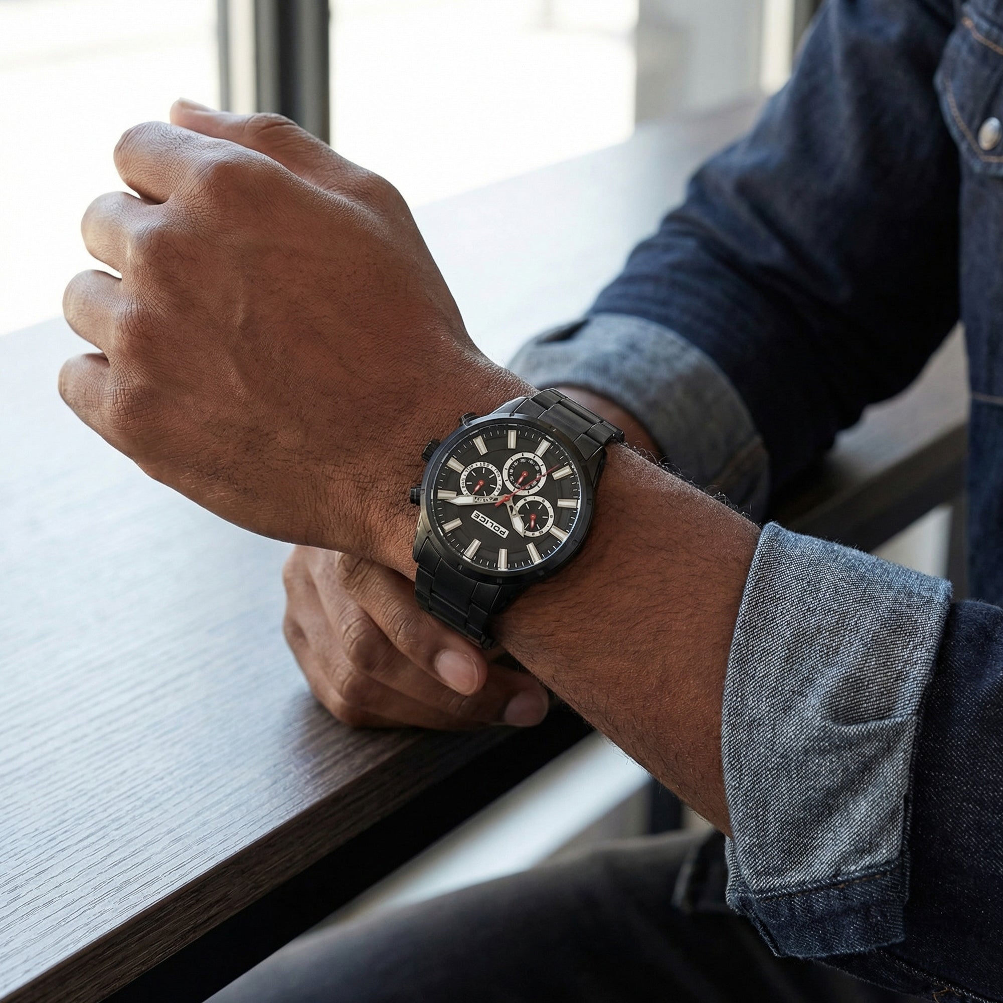 Man in blue denim jacket, sitting at a bench wearing Police Weston all black men's watch.