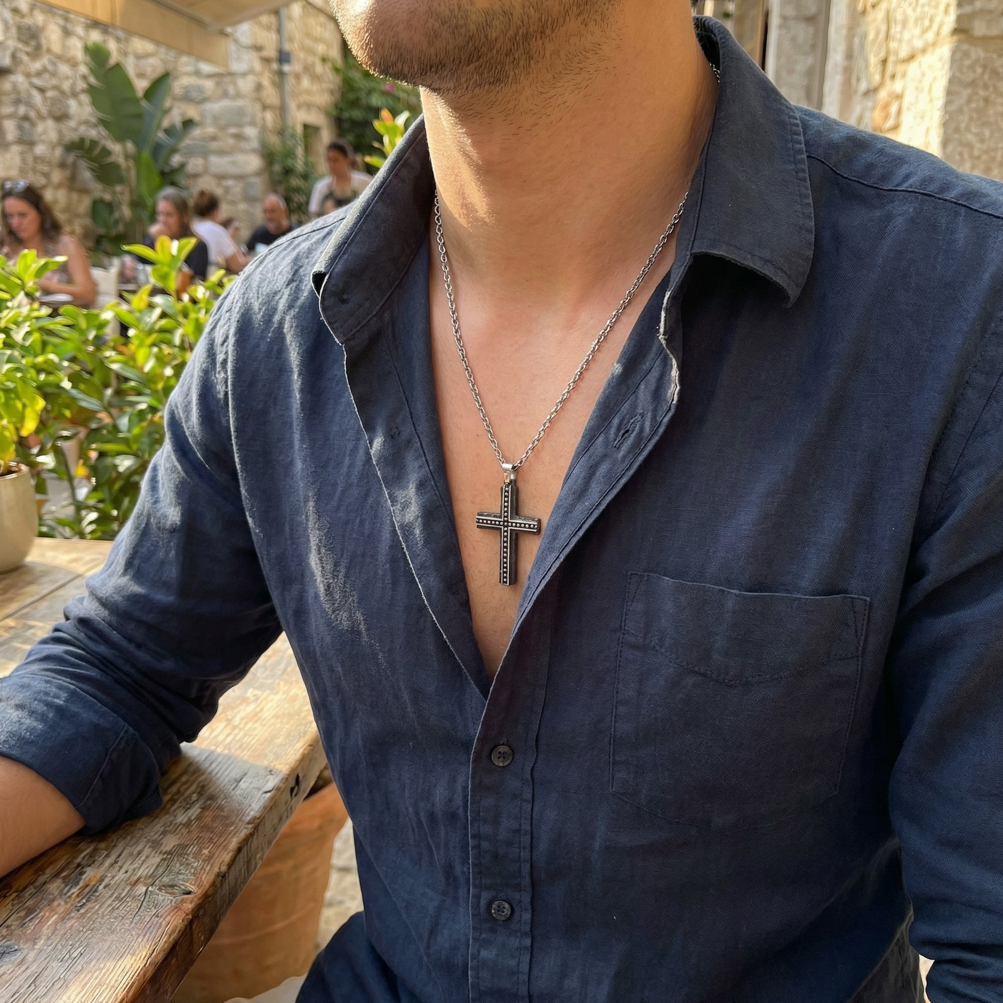Man in a blue open-neck shirt wearing a rough edge black steel cross men's necklace.