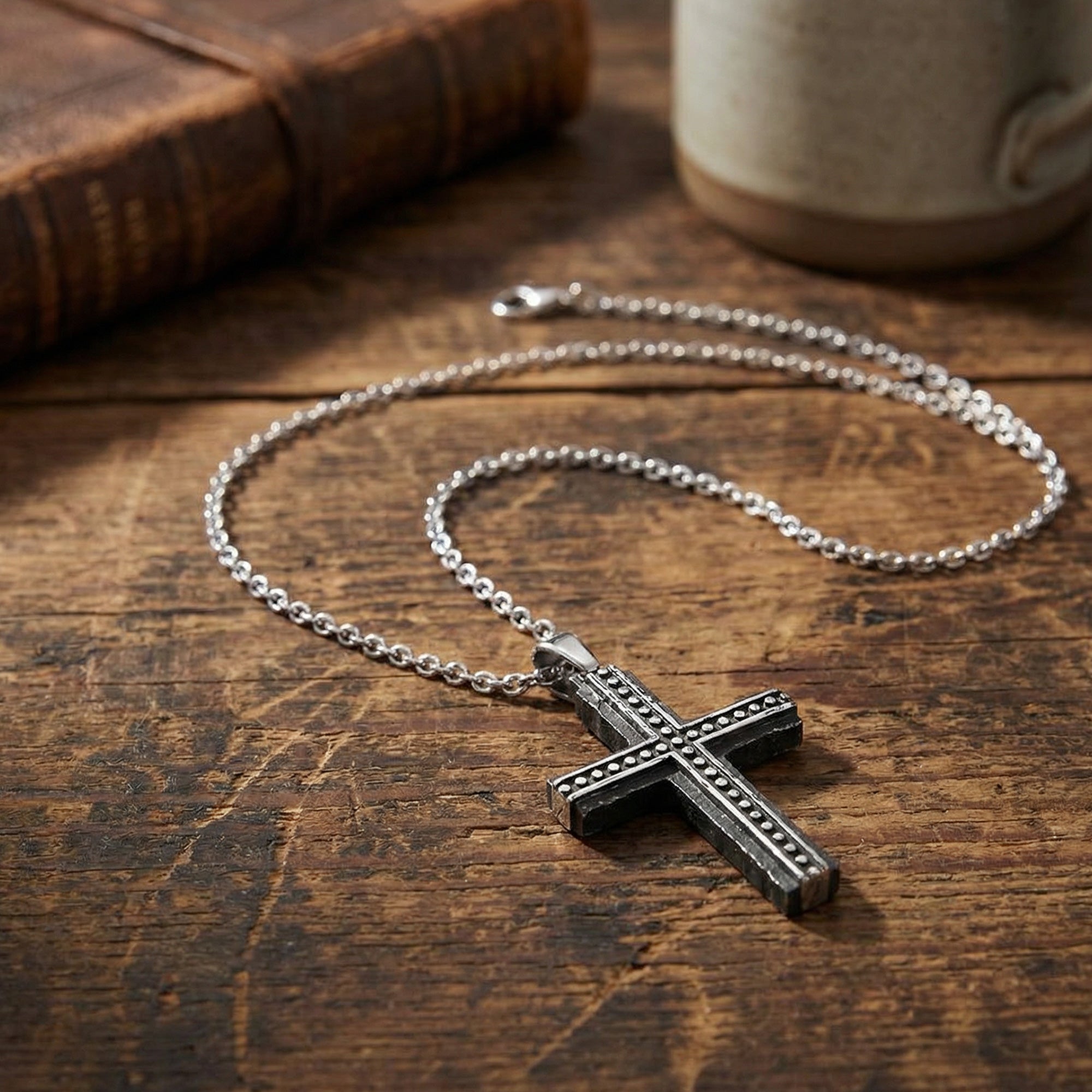 Rough edge black stainless steel cross men's necklace on a wooden table.
