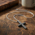 Rough edge black stainless steel cross men's necklace on a wooden table.