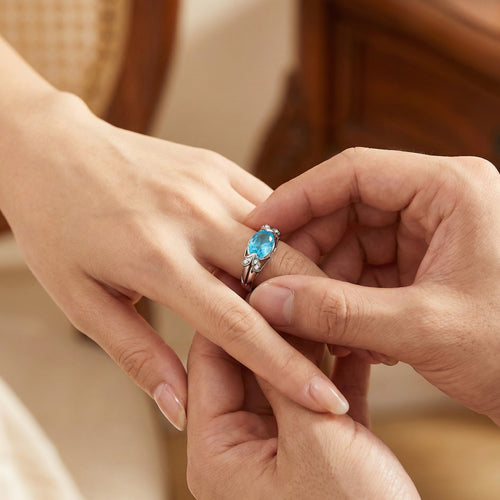 Man placing sterling silver oval cut aquamarine ladies ring on a woman's hand.