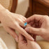 Man placing sterling silver oval cut aquamarine ladies ring on a woman's hand.