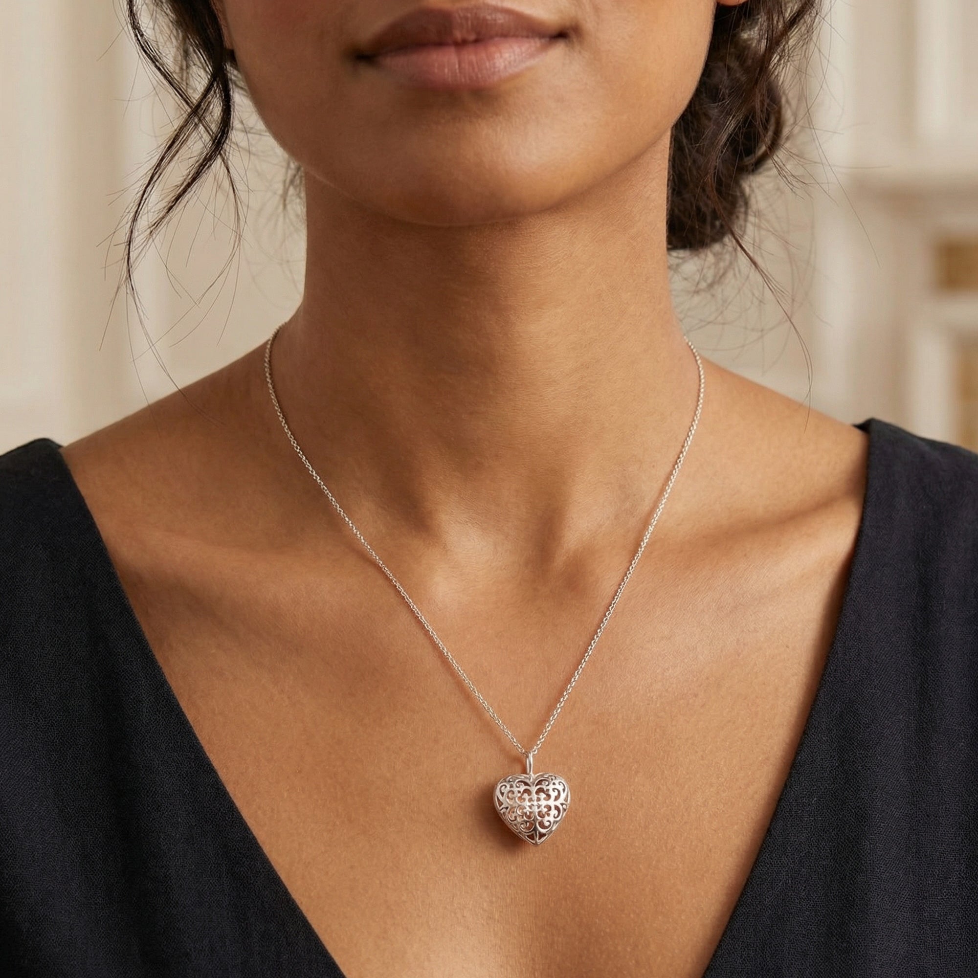 Woman in open-neck blouse wearing an Engelsrufer sterling silver rose gold heart soundball necklace.