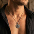 Close-up of young man in open-neck shirt wearing sterling silver men's silver Tibetan vajra cross amulet necklace.