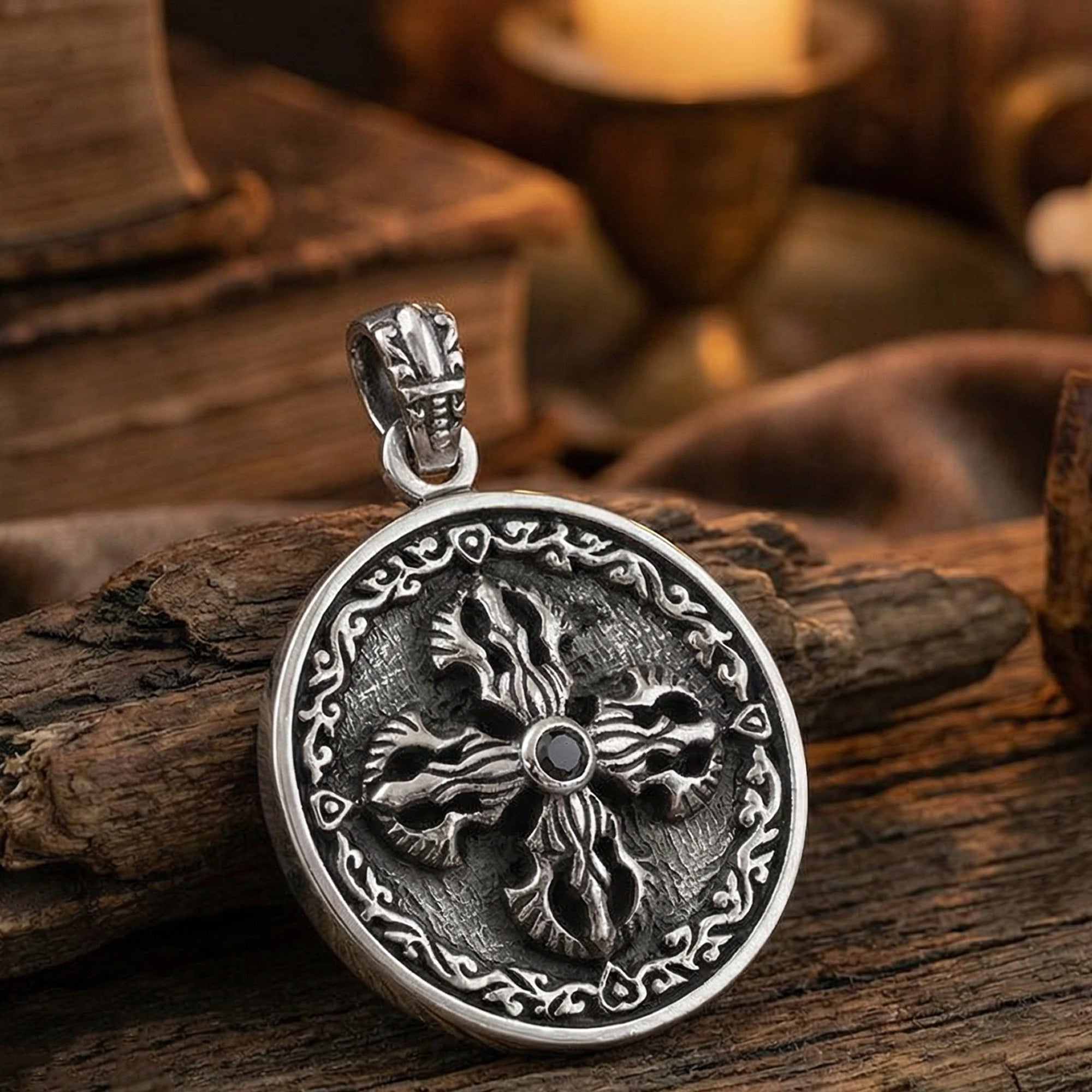 Sterling silver men's silver Tibetan vajra cross amulet pendant on an old wooden table with books and a candle.