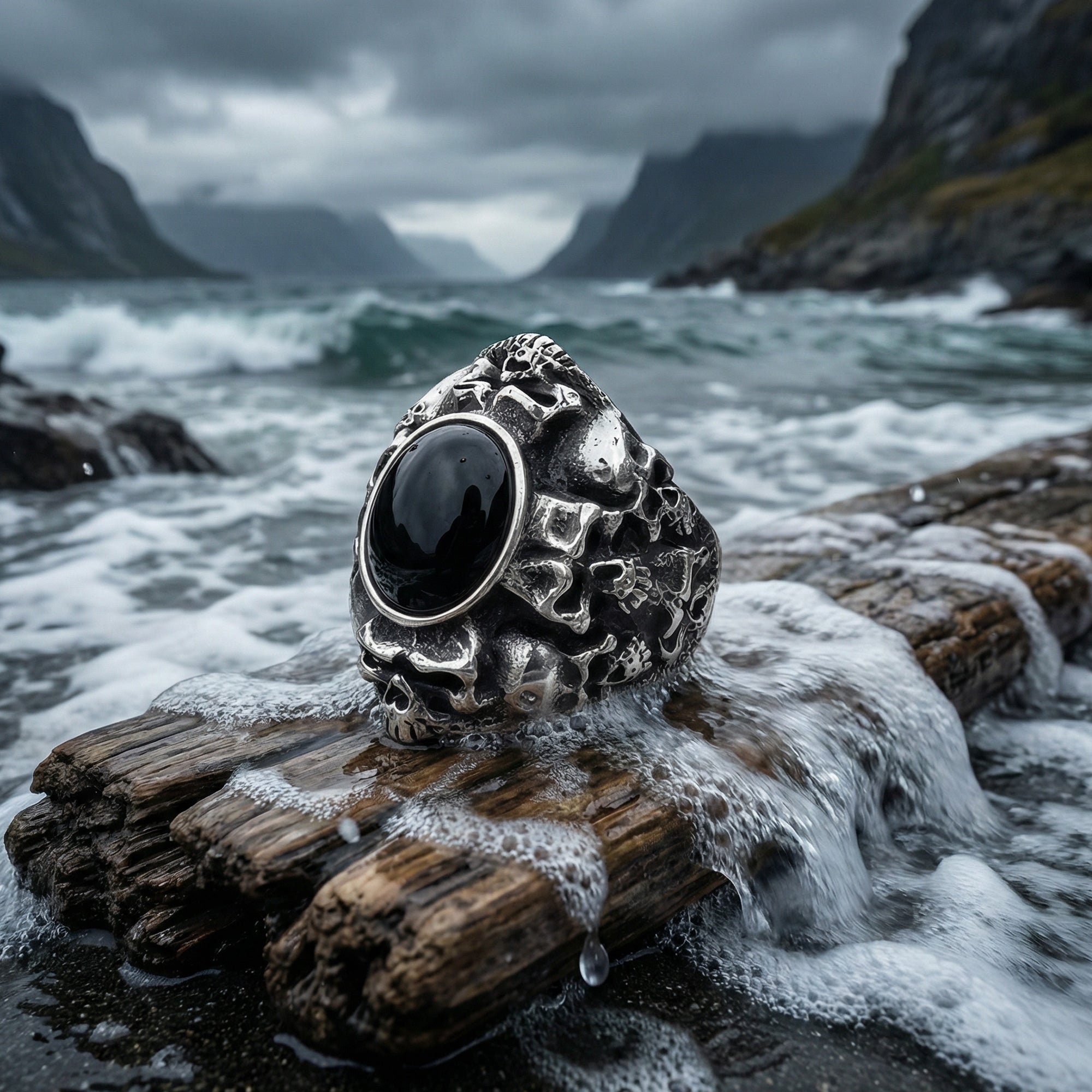 Memento mori skull cluster stainless steel men's ring on a piece of driftwood on the shore as sea water washes over.