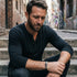 Man sitting on concrete steps wearing a Save Brave skull & dagger men's leather bracelet.