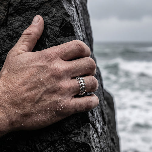 Man's hand gripping a rock while wearing a stainless steel spine vertebrae ring.