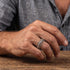 Man in grey open-neck shirt wearing a stainless steel spine vertebrae ring.