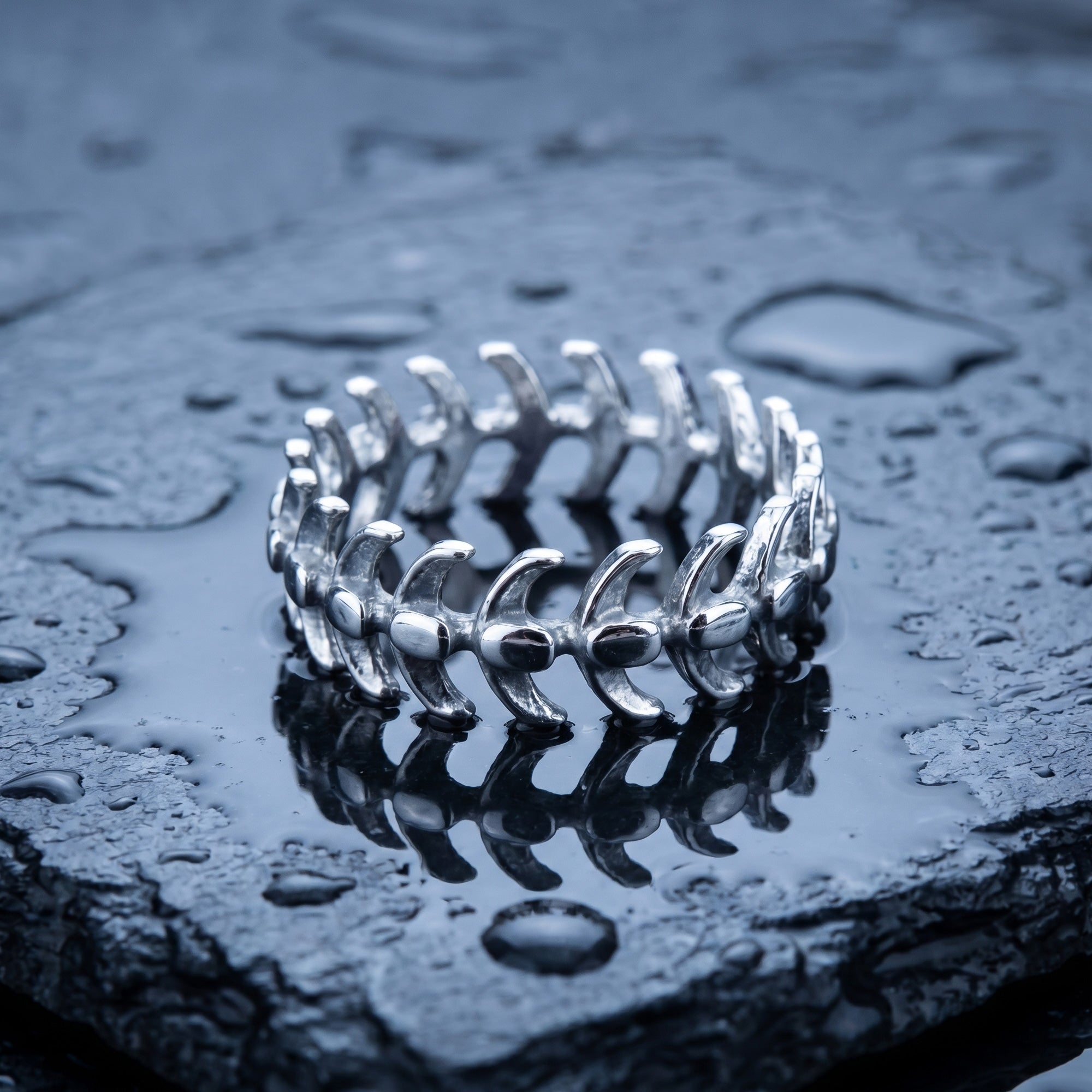 Stainless steel men's spine vertebrae ring laying on a wet piece of black slate.
