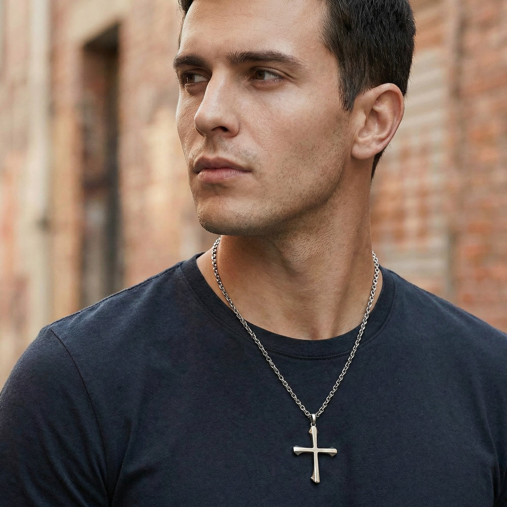 Young man in a t-shirt looking left while wearing barbed cross stainless steel necklace.