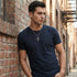 Young man leaning against a brick wall wearing barbed cross stainless steel necklace.
