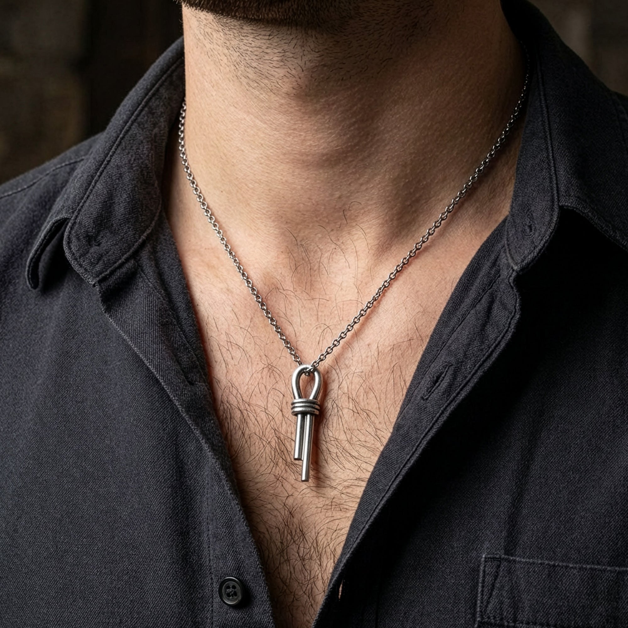 Close-up of a man in an open-neck shirt wearing a sterling silver nautical scaffold knot men's necklace.