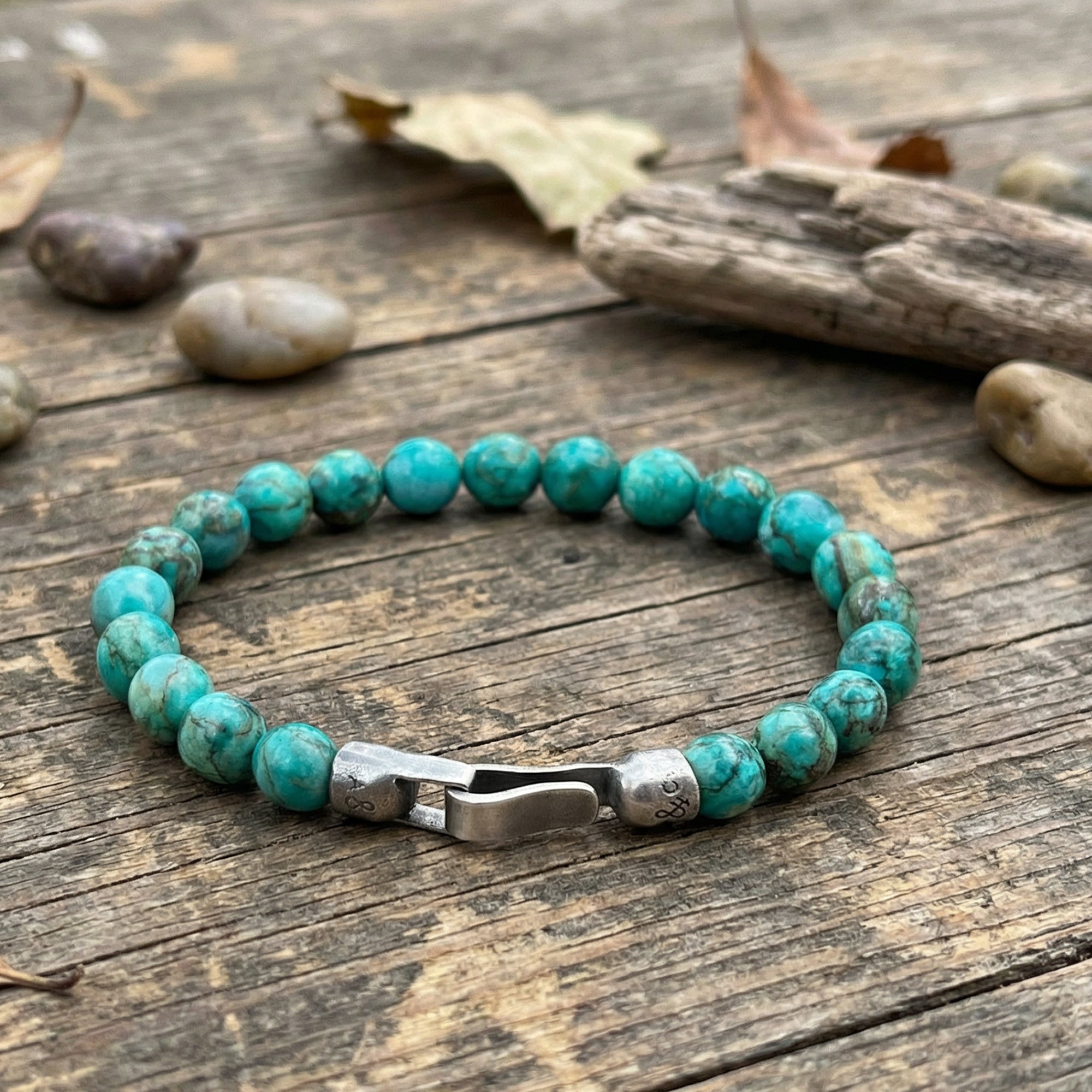 Anchor & Crew Nachi sterling silver blue turquoise stone bracelet on outdoor wood surface with rocks and leaves.