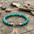 Anchor & Crew Nachi sterling silver blue turquoise stone bracelet on outdoor wood surface with rocks and leaves.